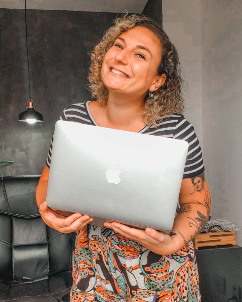 Nicole em seu homeoffice, sorrindo com o macbook na mão.